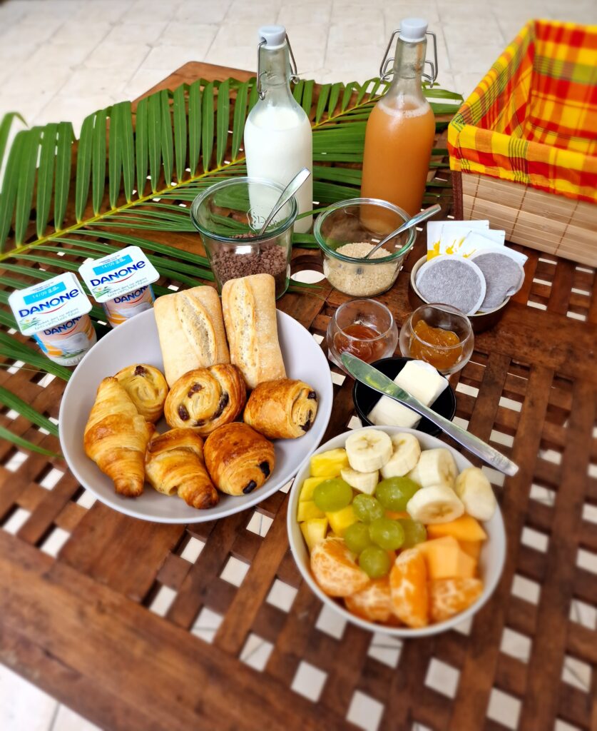 Petit-déjeuner créole La Kaz Mangococo avec viennoiseries, fruits frais et jus, servi en terrasse en Guadeloupe